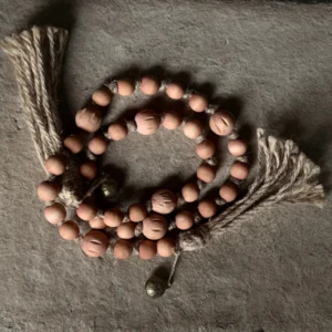 Een decoratieve bohemian stijl houten kralen ketting met roze kralen en jute klosjes met belletjes.