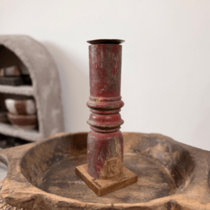 Oude houten baluster kandelaar met rood doorleefd patina, geplaatst op een houten schaal in een sober landelijk interieur